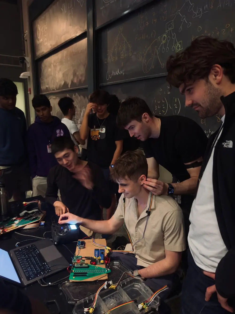 Students crowd around a live EEG demo in a chalkboard classroom
