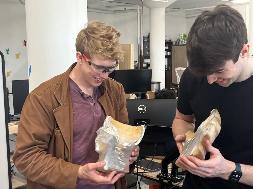 Two engineers grinning over halves of a cut-open skull phantom